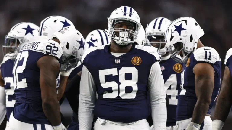 Football players in blue and white uniforms, reminiscent of the Cowboys, huddle on the field during a game.